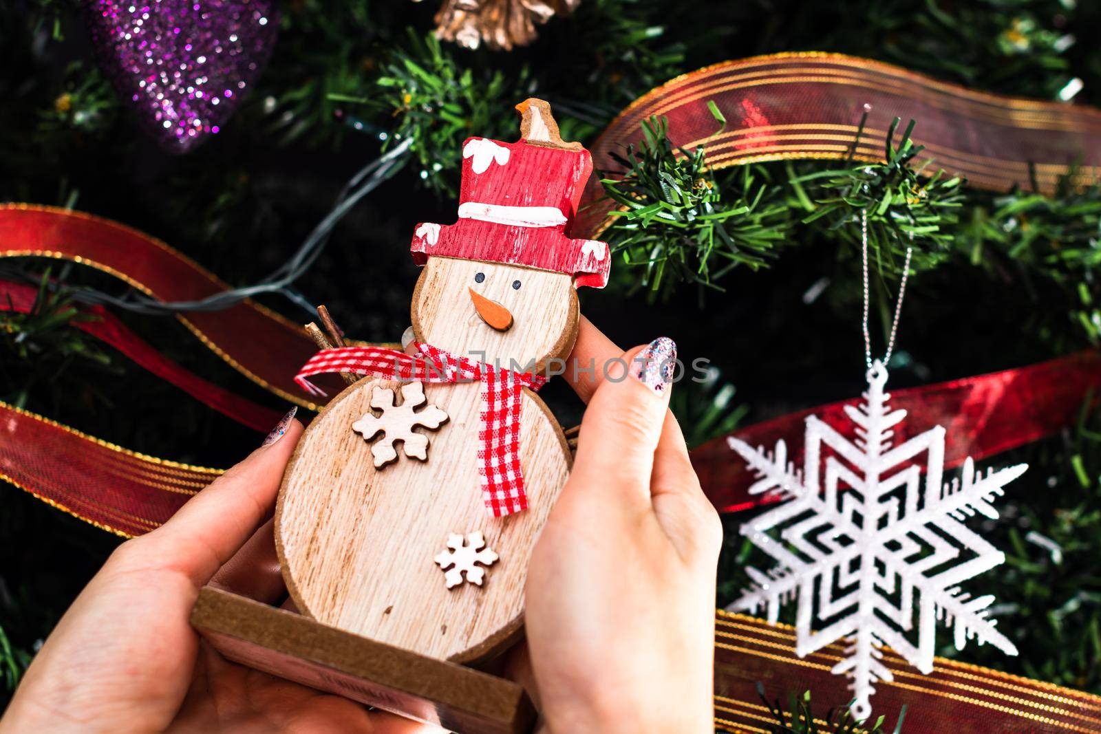 Hands holding Christmas snowman figurine in front of the Christmas tree. Decorating the fir tree isolated by vladispas