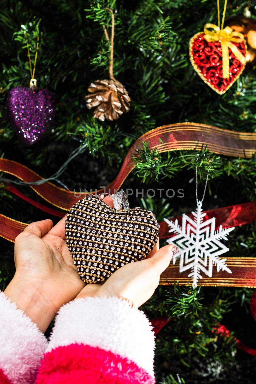 Hands holding Christmas ornament in front of Christmas tree. Decorating fir branches with Christmas decorations. by vladispas