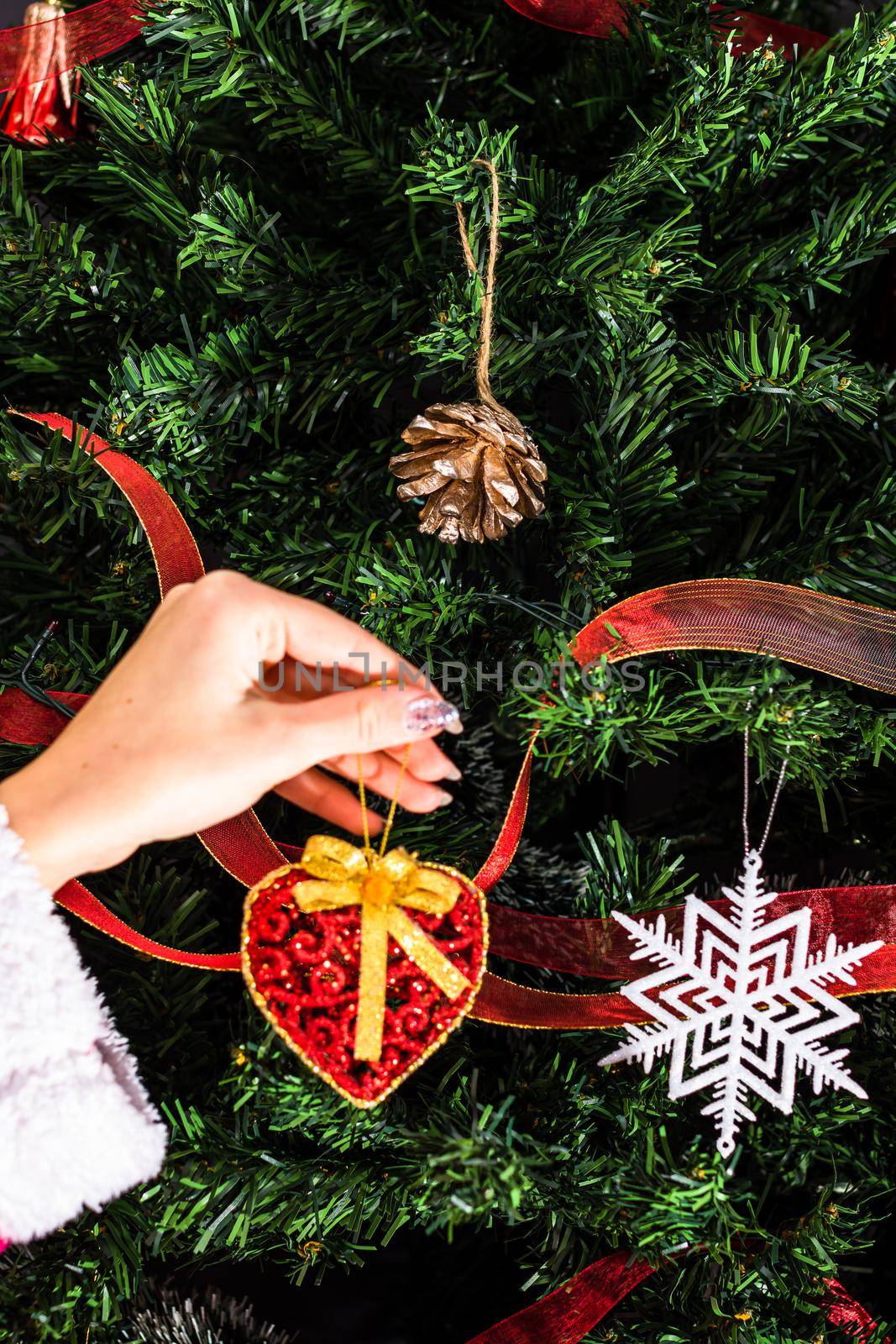 Decorating Christmas tree, hand putting Christmas decorations on fir branches. Christmas hanging decorations.