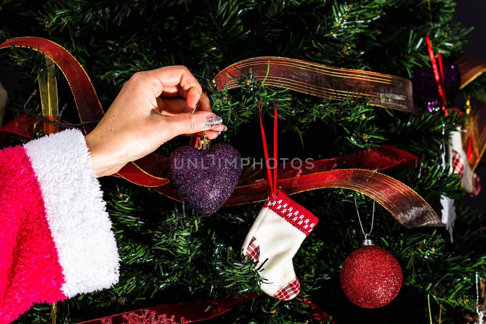 Decorating Christmas tree, hand putting Christmas decorations on fir branches. Christmas hanging decorations.