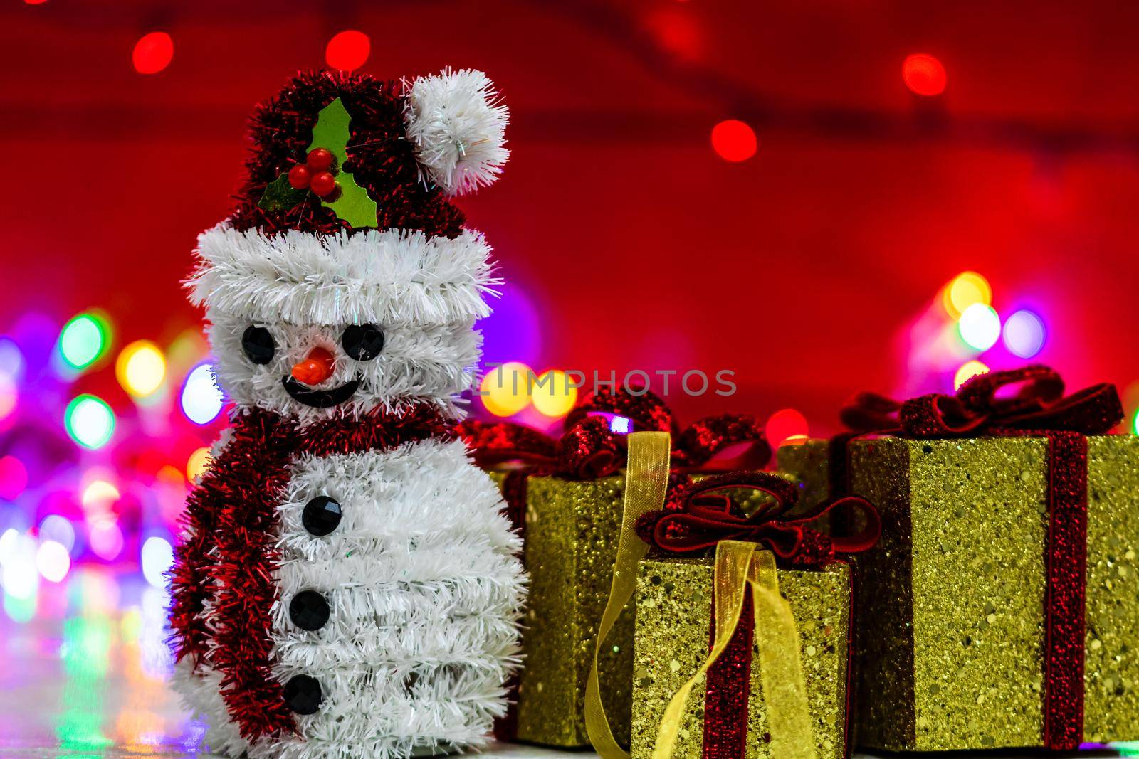 Snowman Christmas figurine near glittery gifts isolated on blurred background of lights. Christmas decorations isolated by vladispas