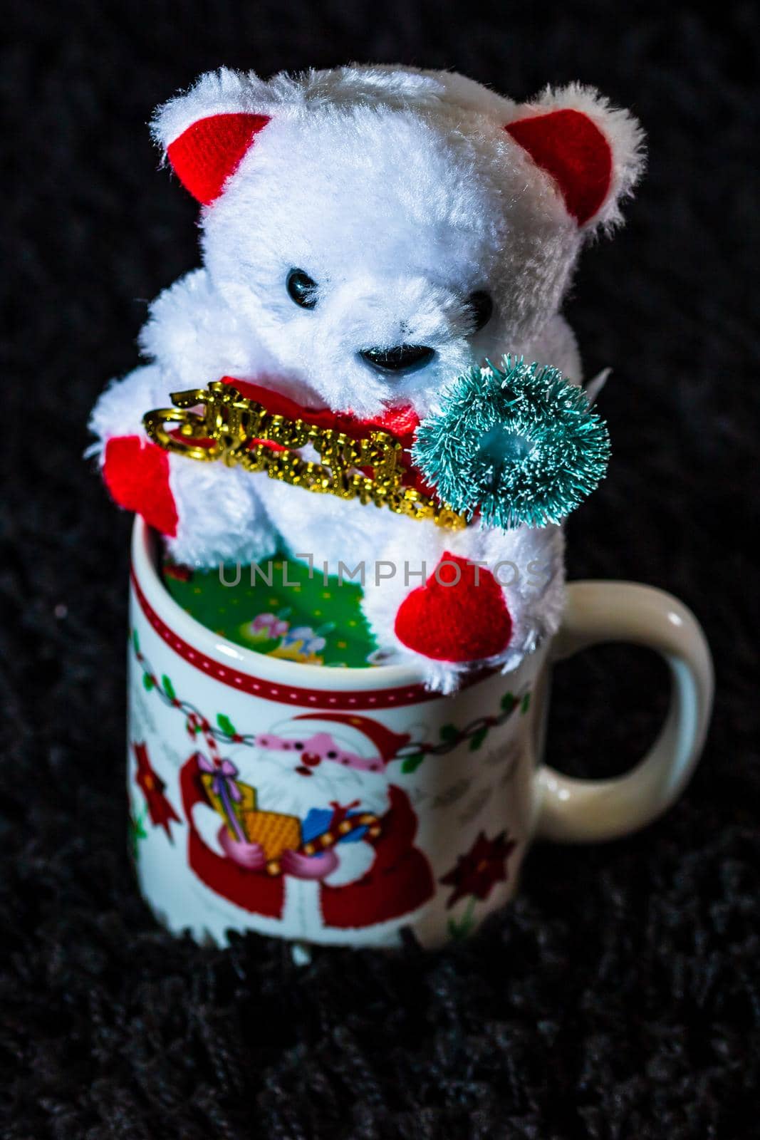 Decorated teddy bear in a Christmas cup isolated on black.  Bucharest, Romania, 2020. by vladispas