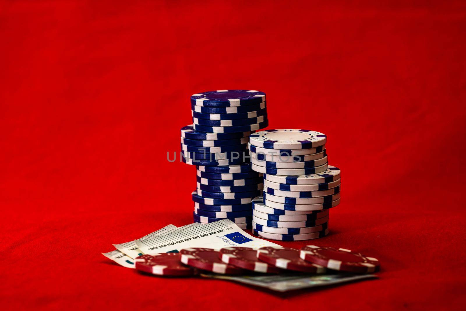 Stacks of poker chips with money on red background, EURO currency by vladispas