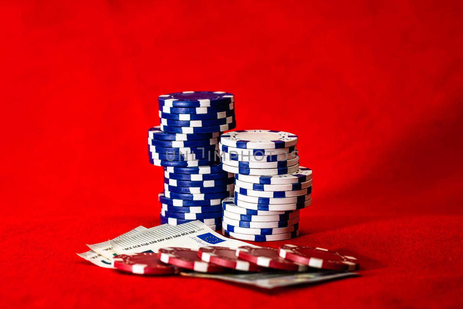 Stacks of poker chips with money on red background, EURO currency by vladispas