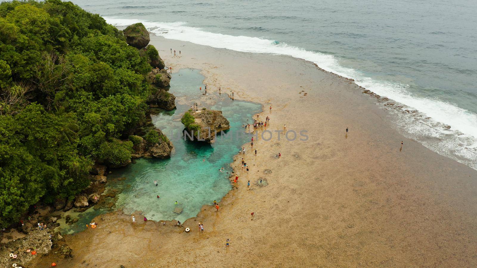 Rocky shore at low tide with swimming pools and tourists. Magpupungko natural rock pools. Siargao, Philippines.