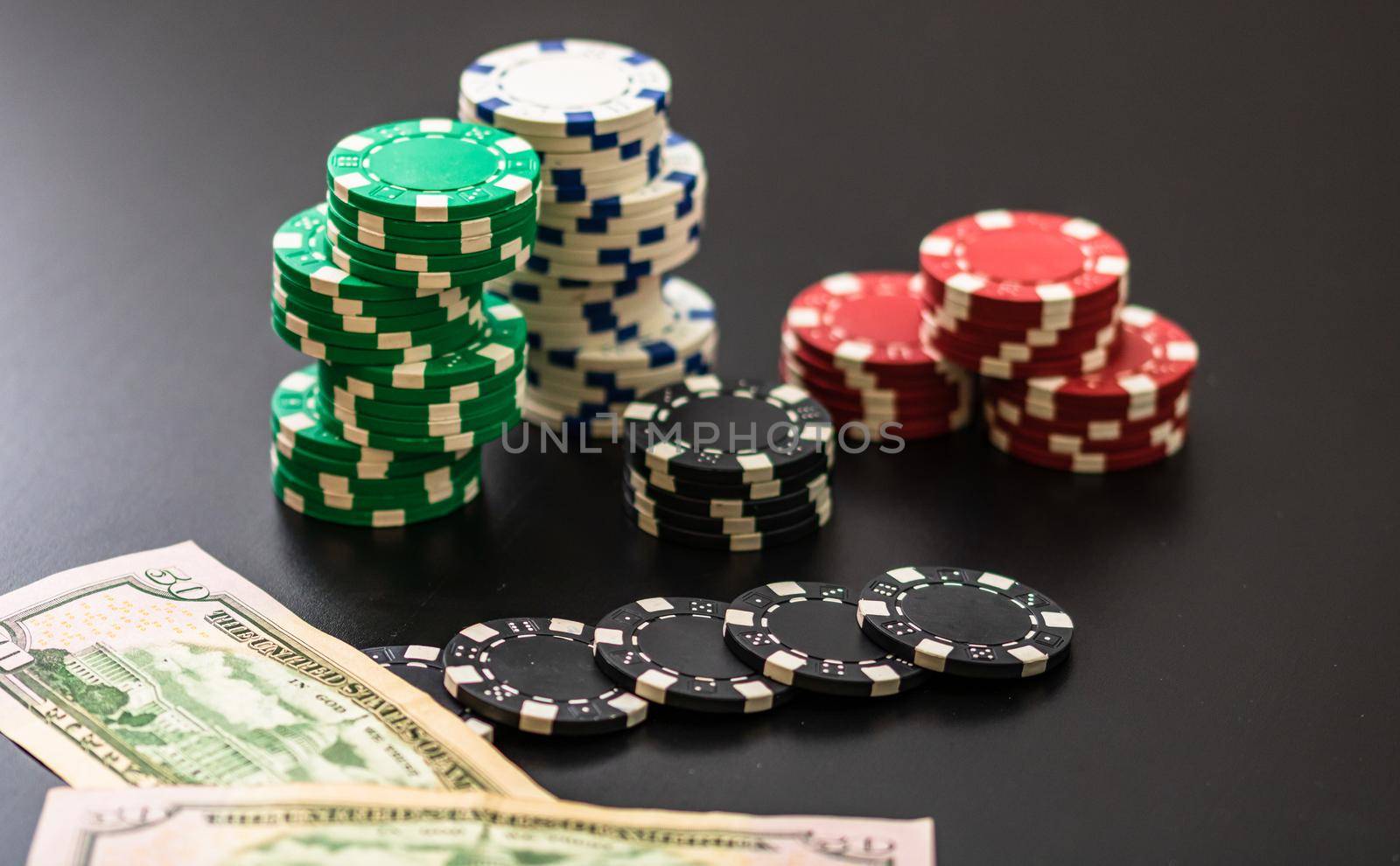 Stacks of poker chips and dollar bills on black background. Poker concept, chips and money. by vladispas