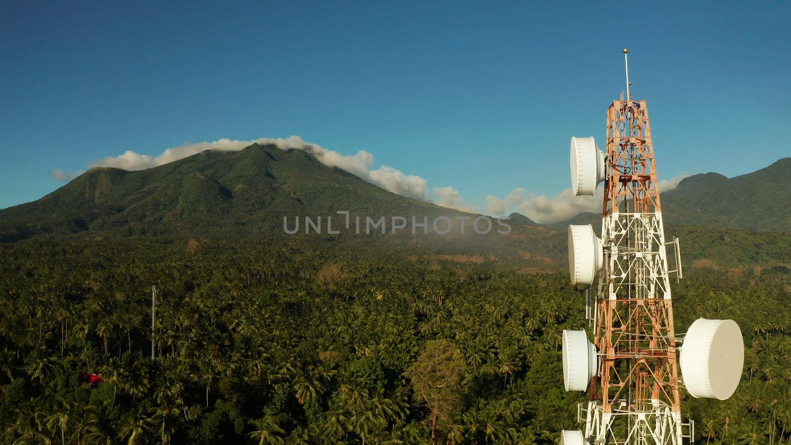Telecommunication tower, communication antenna against mountains and rainforest, aerial view. Repeaters on a metal tower. Camiguin, Philippines