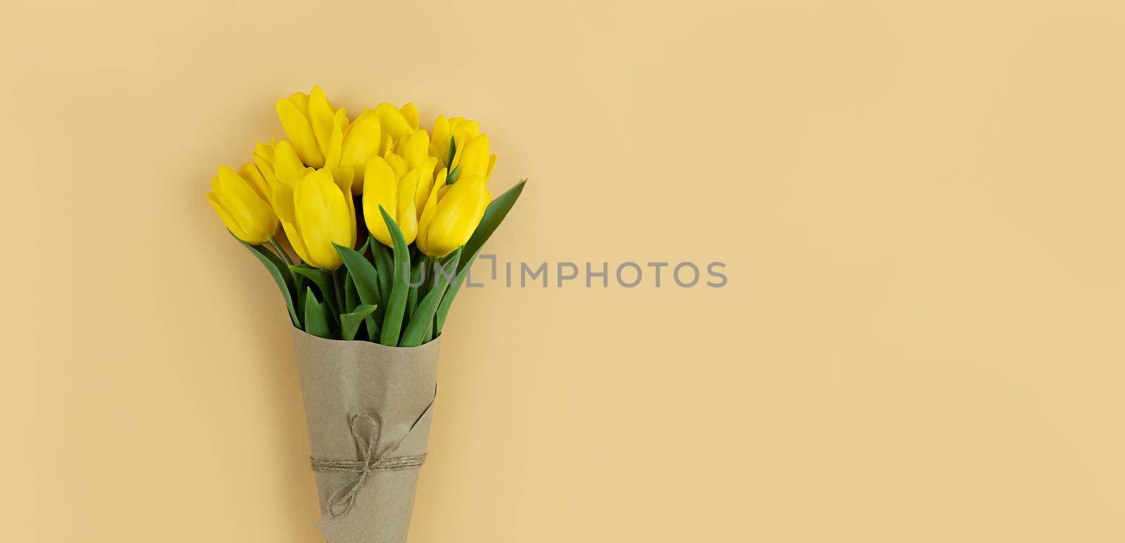 Bouquet of yellow tulips wrapped in craft paper on a beige background with copyspace.