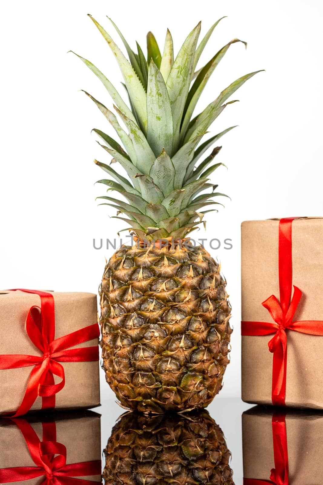 Fresh pineapple fruit and square gift boxes in craft paper on black glass table on white background