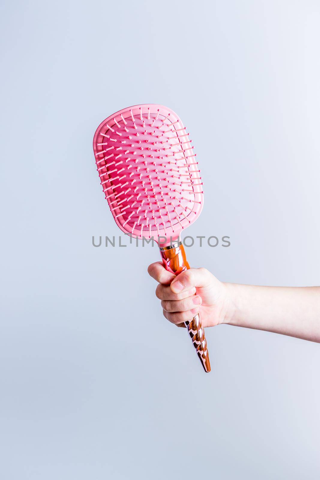 Beautiful pink comb brush in the hand of a girl on a white background vertical. Women's Hair Care Accessories. Side view