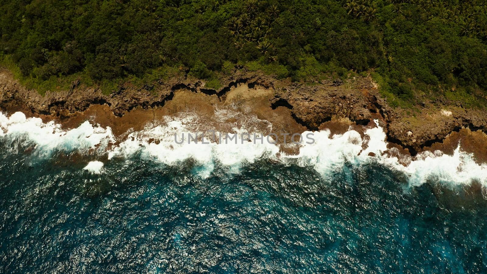 Waves of the blue ocean crashing against the shore and rocks. Siargao, Philippines. Summer and travel vacation concept