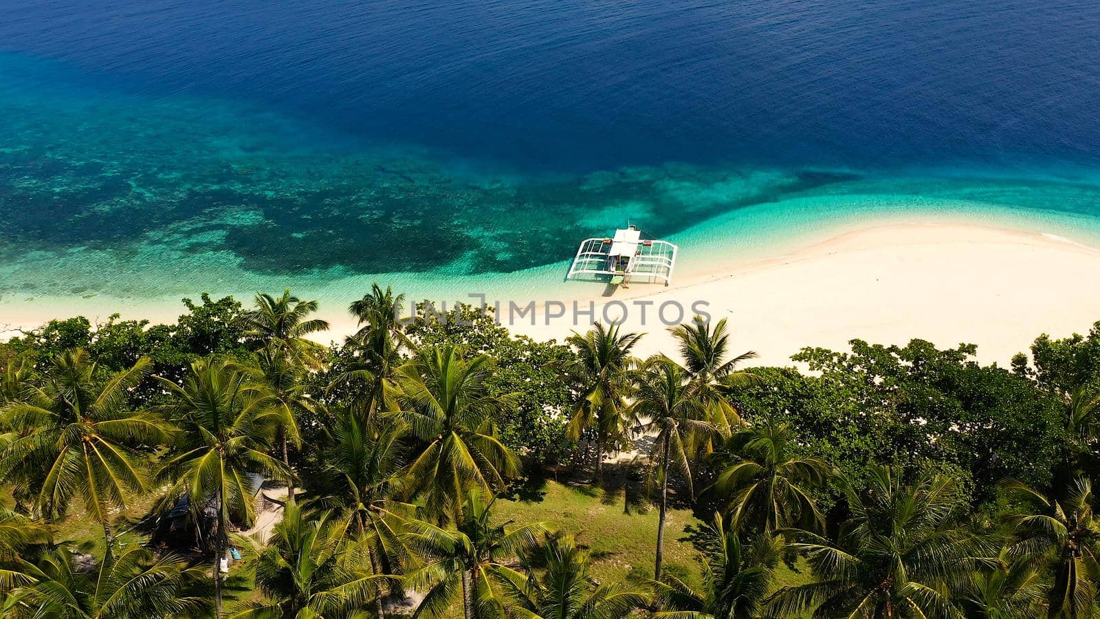 Tropical beach of white sand, top view. Tourist boat off the coast. Blue sea with turquoise lagoons. Summer and travel vacation concept. Tranquil beach scene.