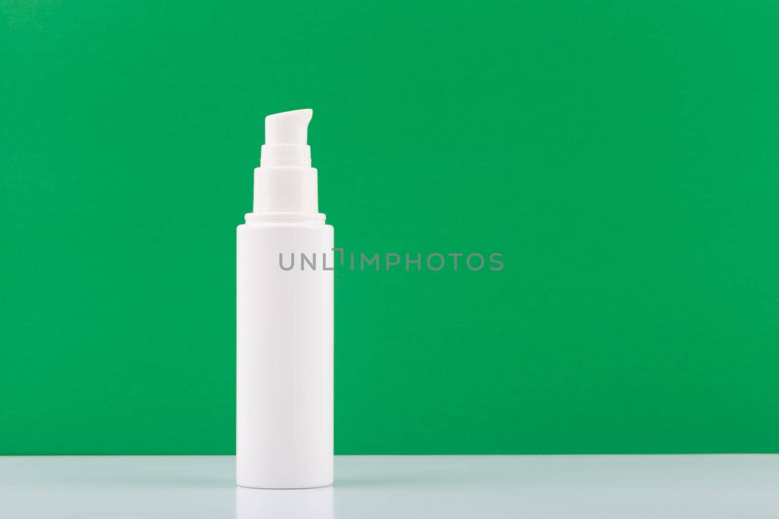 White cream or lotion tube on white glossy table against green background with copy space. Concept of organic cosmetic with natural ingredients