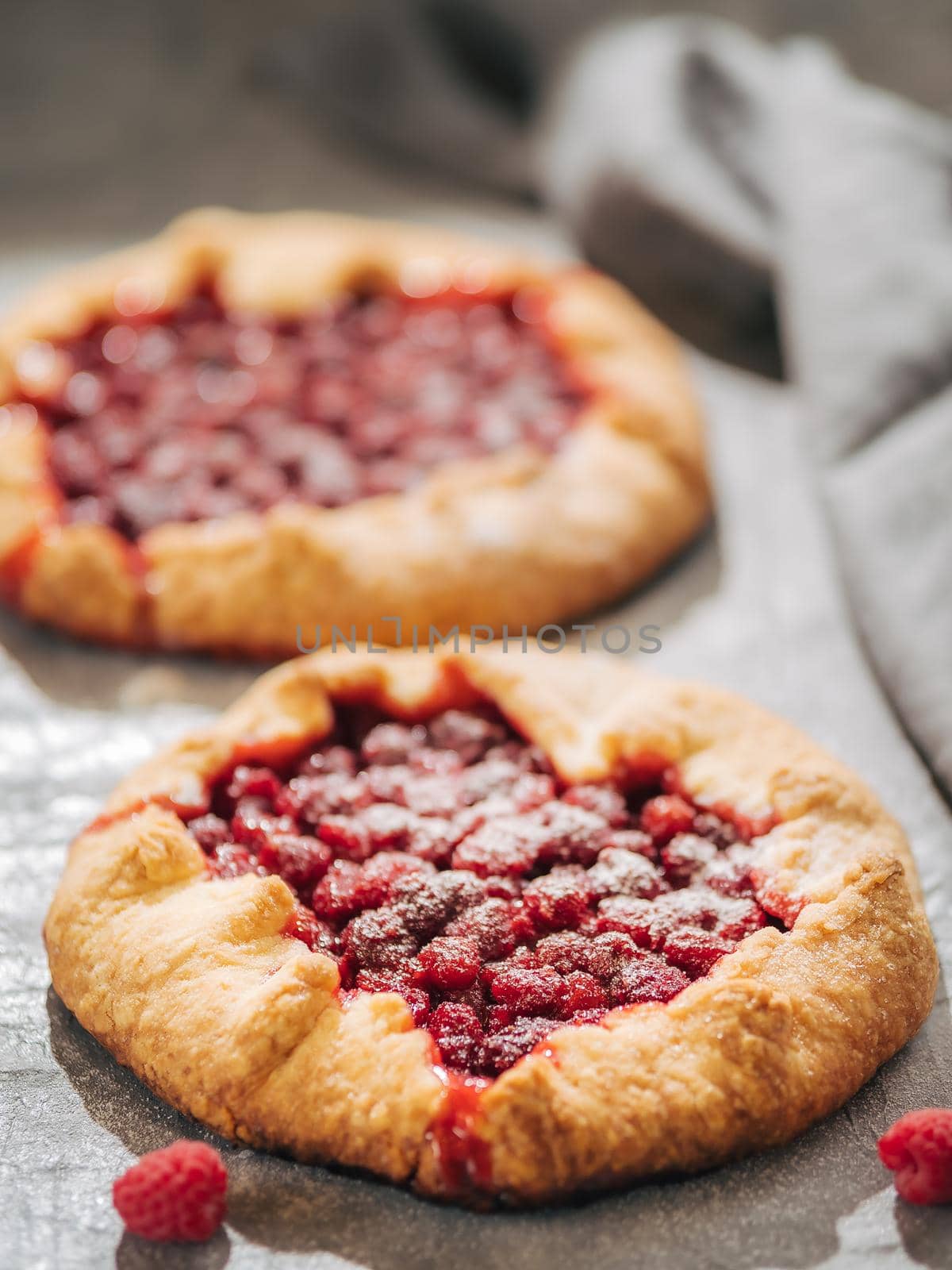 Two perfect raspberry galettes. Delicious rustic homemade tart with frozen or fresh raspberries on gray background. Beautiful round shape galettes with raspberries, copy space. Vertical. Shallow DOF