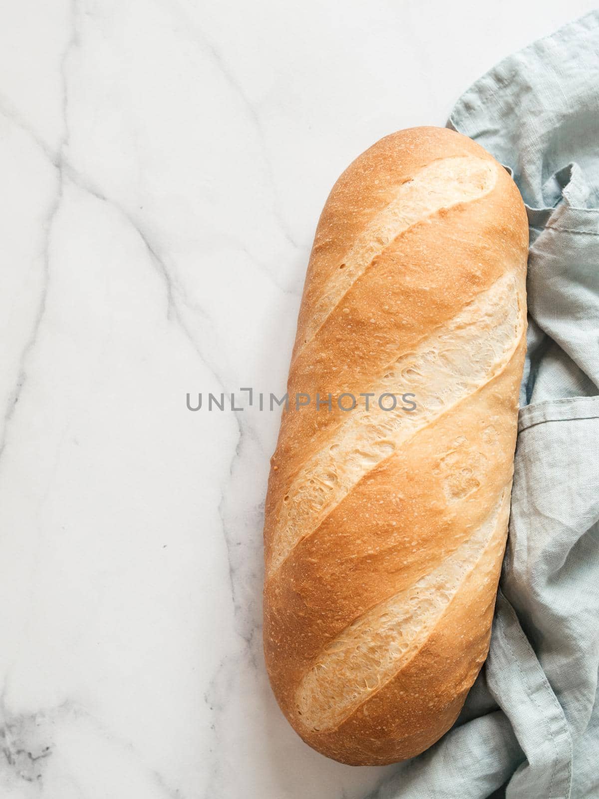 British White Bloomer or European Baton loaf bread on white marble background. Top view or flat lay. Copy space for text or design. Vertical.