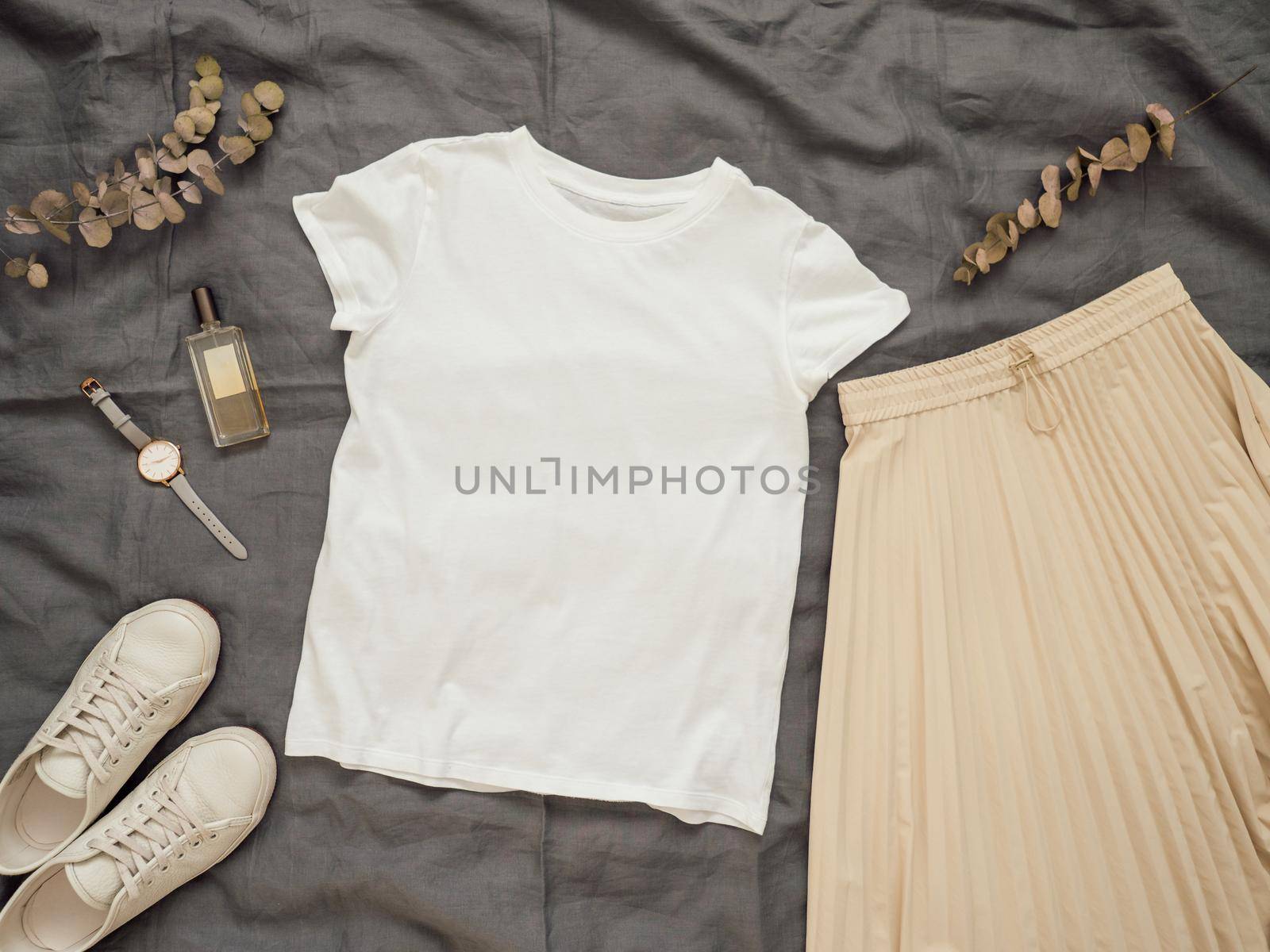 Fashionable female look with white empty t-shirt, cream pleated skirt and white sneakers. Top view of white blank t-shirt with short sleeves over gray bed linen. Mock up for t-shirt print design.