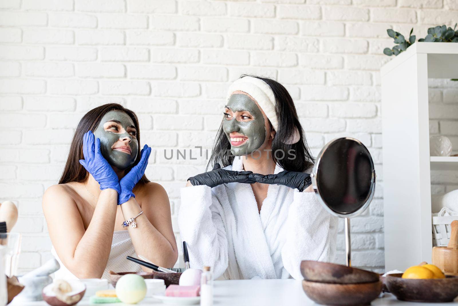 two beautiful women in gloves applying facial mask having fun by Desperada