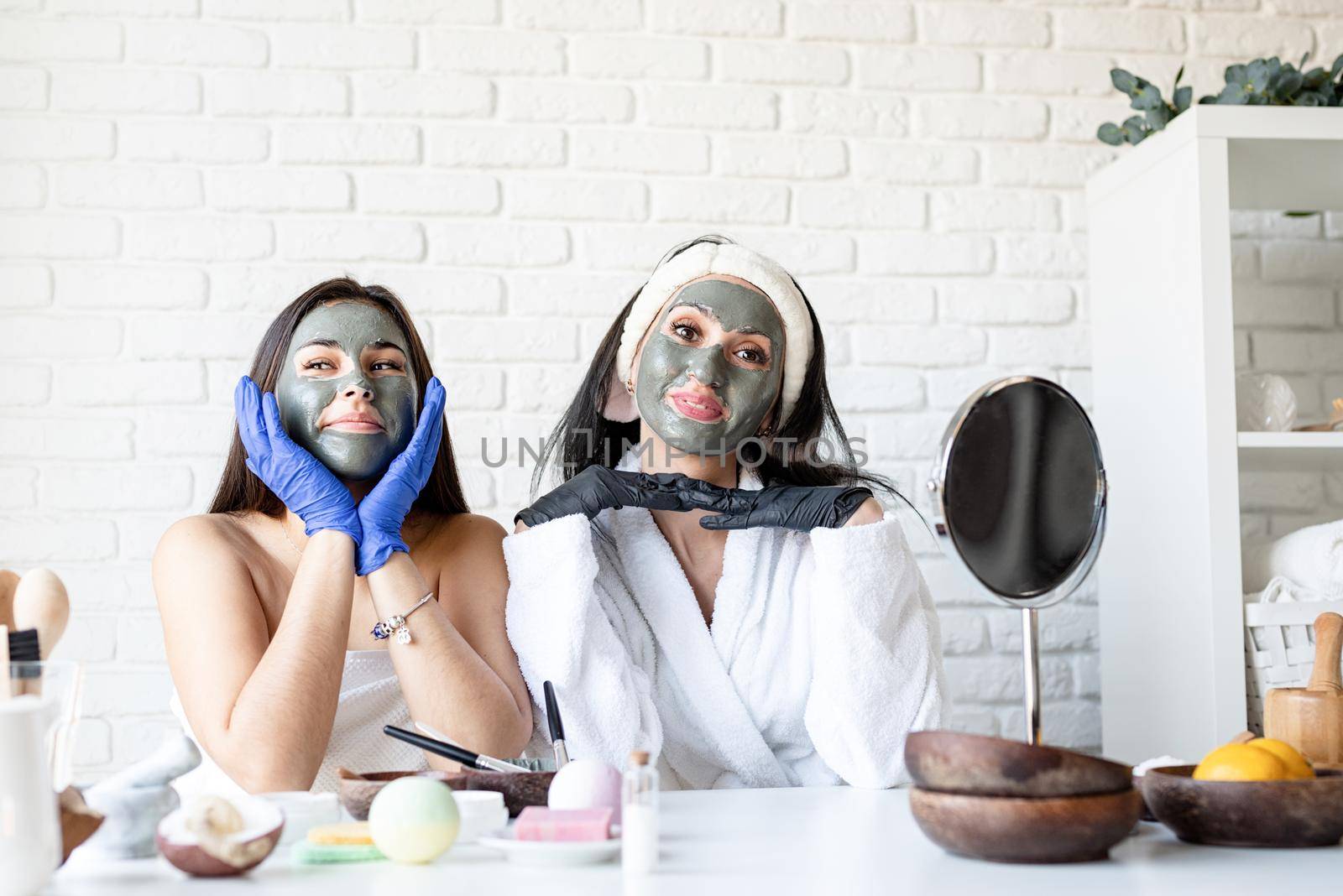 two beautiful women in gloves applying facial mask having fun by Desperada