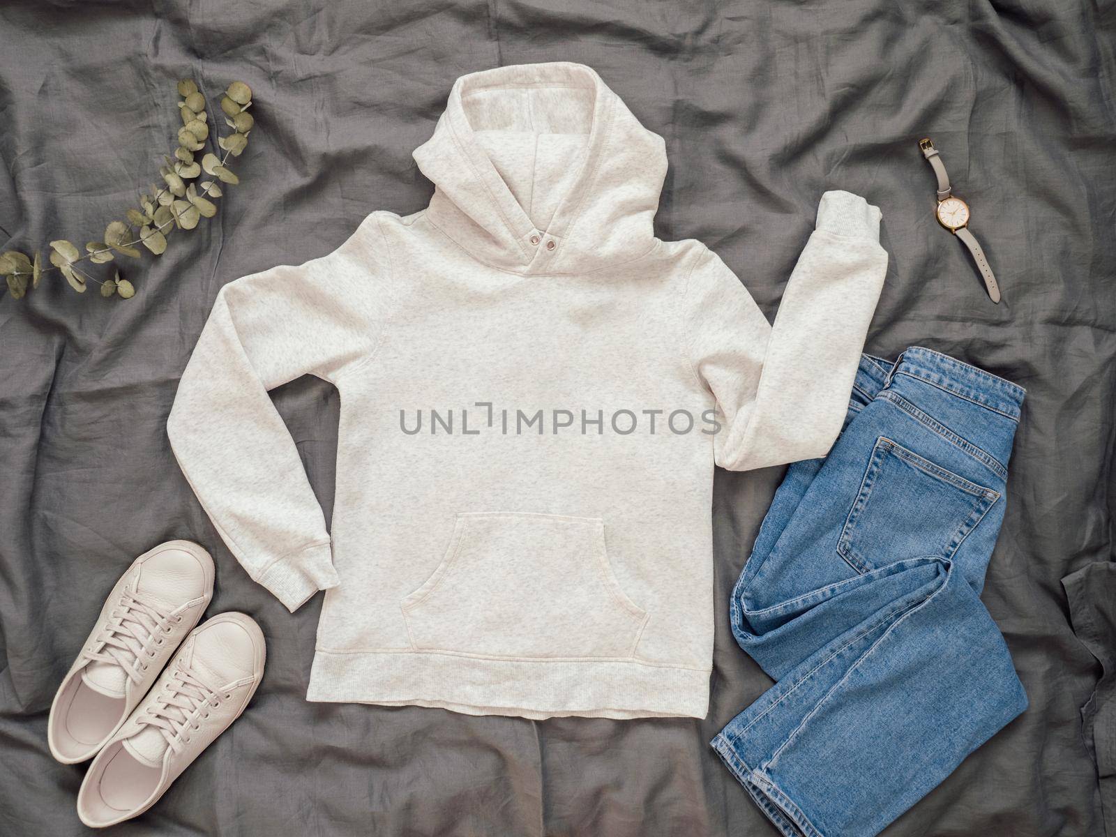 Fashionable look with white empty hoody, jeans and white sneakers. Top view of white blank hoody with long sleeves over gray bed linen. Mock up for hoody print design.
