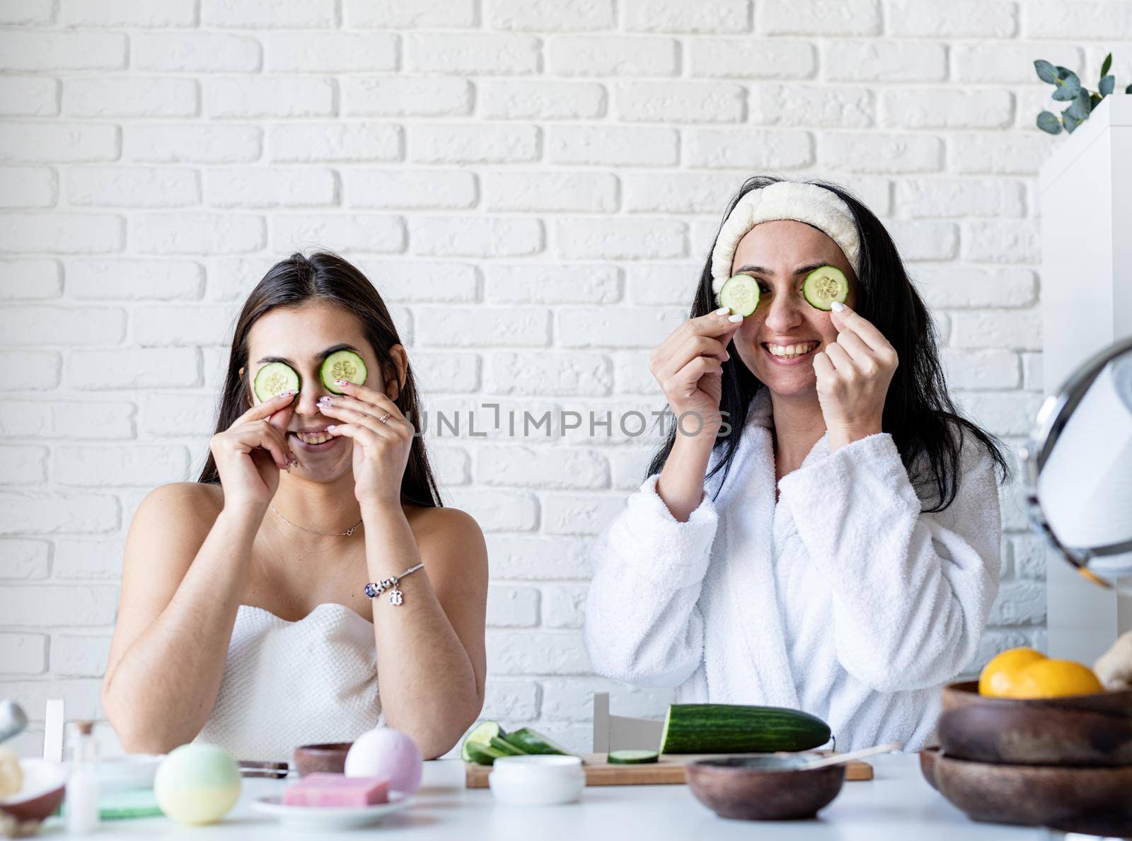 two beautiful women doing spa procedures covering eyes with cucumbers by Desperada