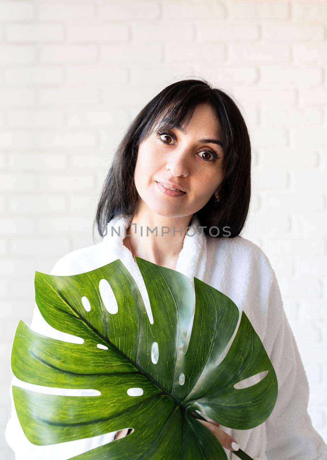 Happy beautiful middle eastern woman wearing bath towels holding a green monstera leaf by Desperada