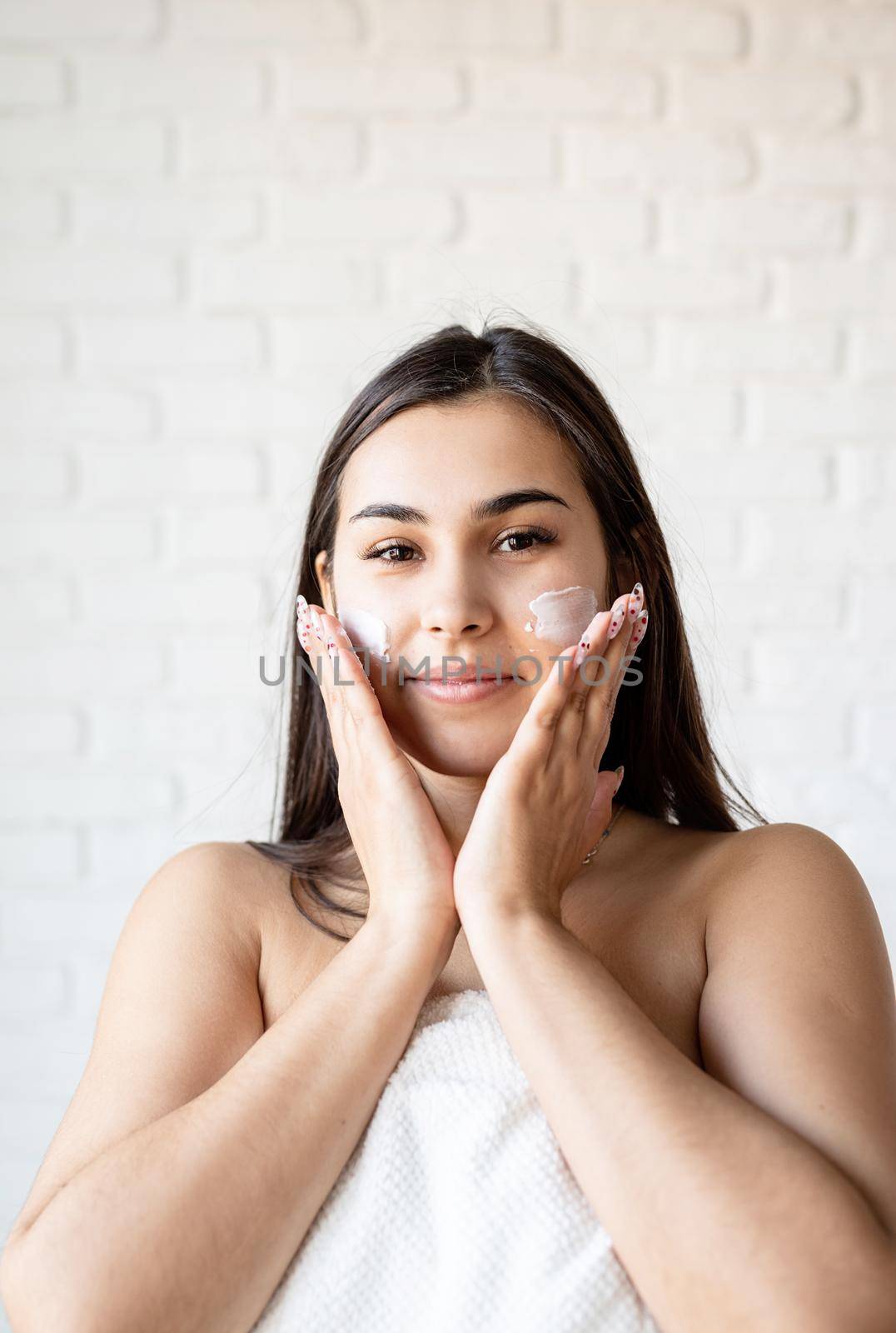 Happy beautiful woman wearing bath robes applying facial cream on her face by Desperada