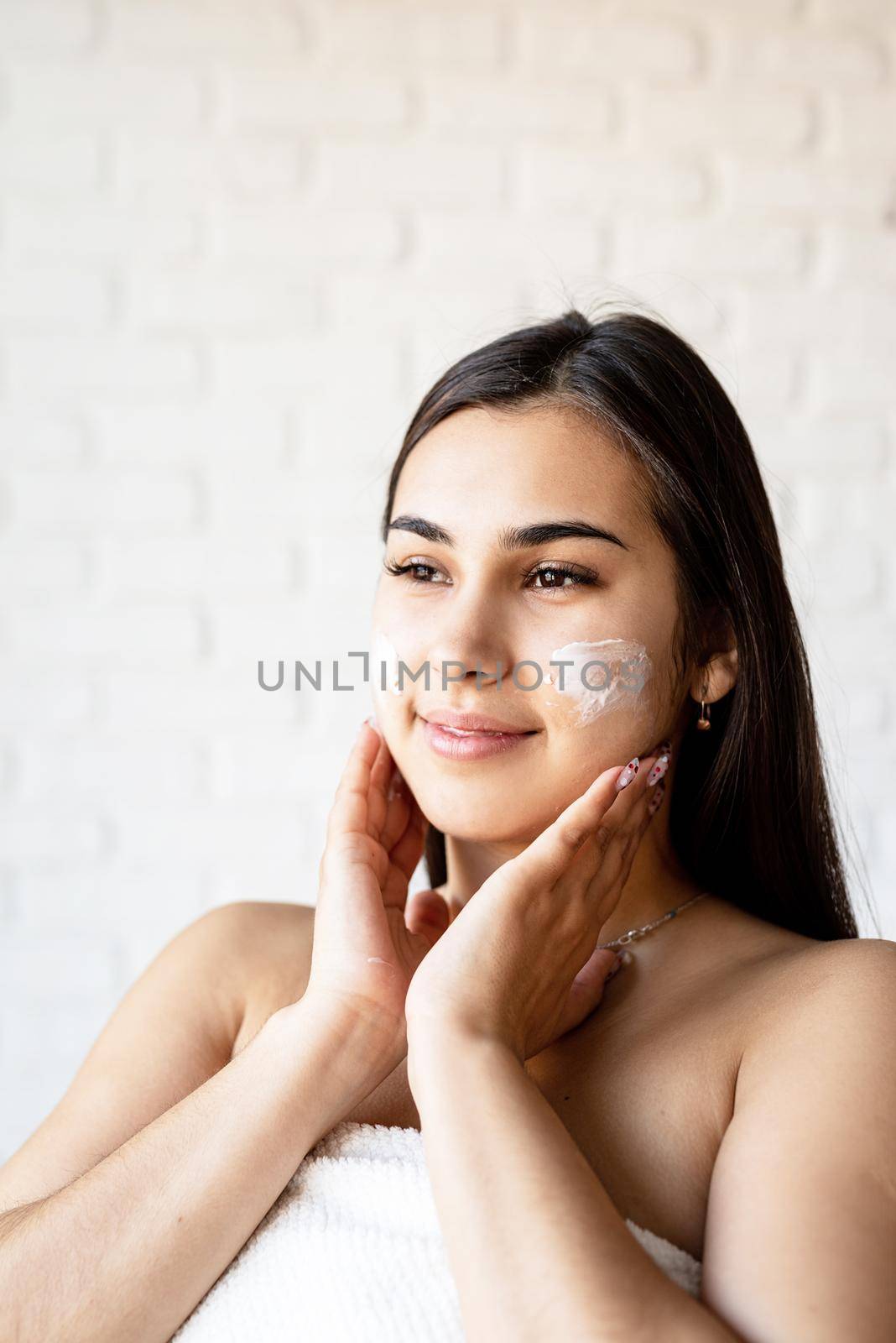 Spa and beauty. Happy beautiful caucasian woman wearing bath robes applying facial cream on her face