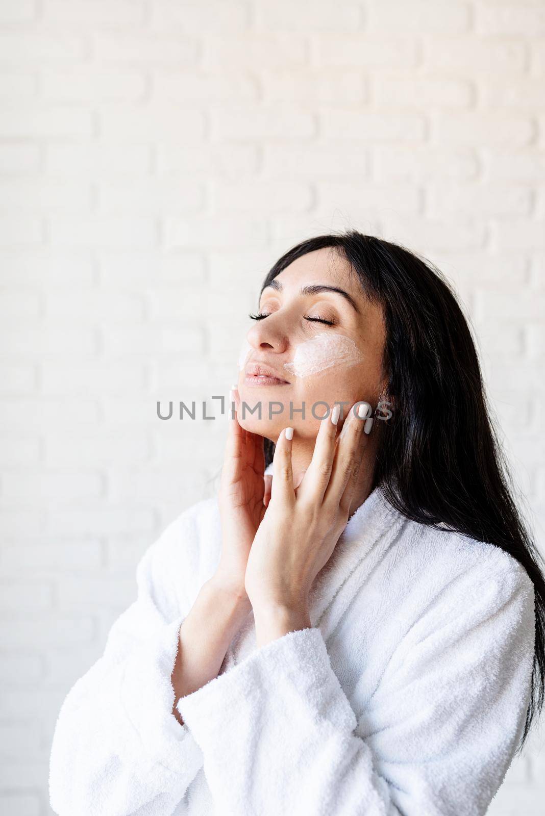 Spa and beauty. Happy beautiful middle eastern woman wearing bath towels applying facial cream on her face