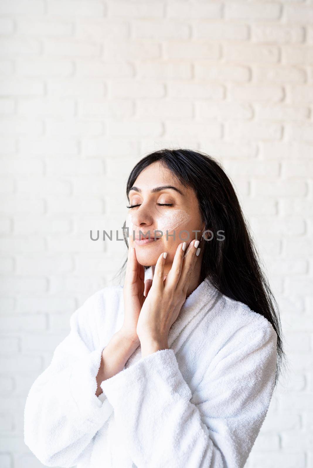 Spa and beauty. Happy beautiful middle eastern woman wearing bath towels applying facial cream on her face