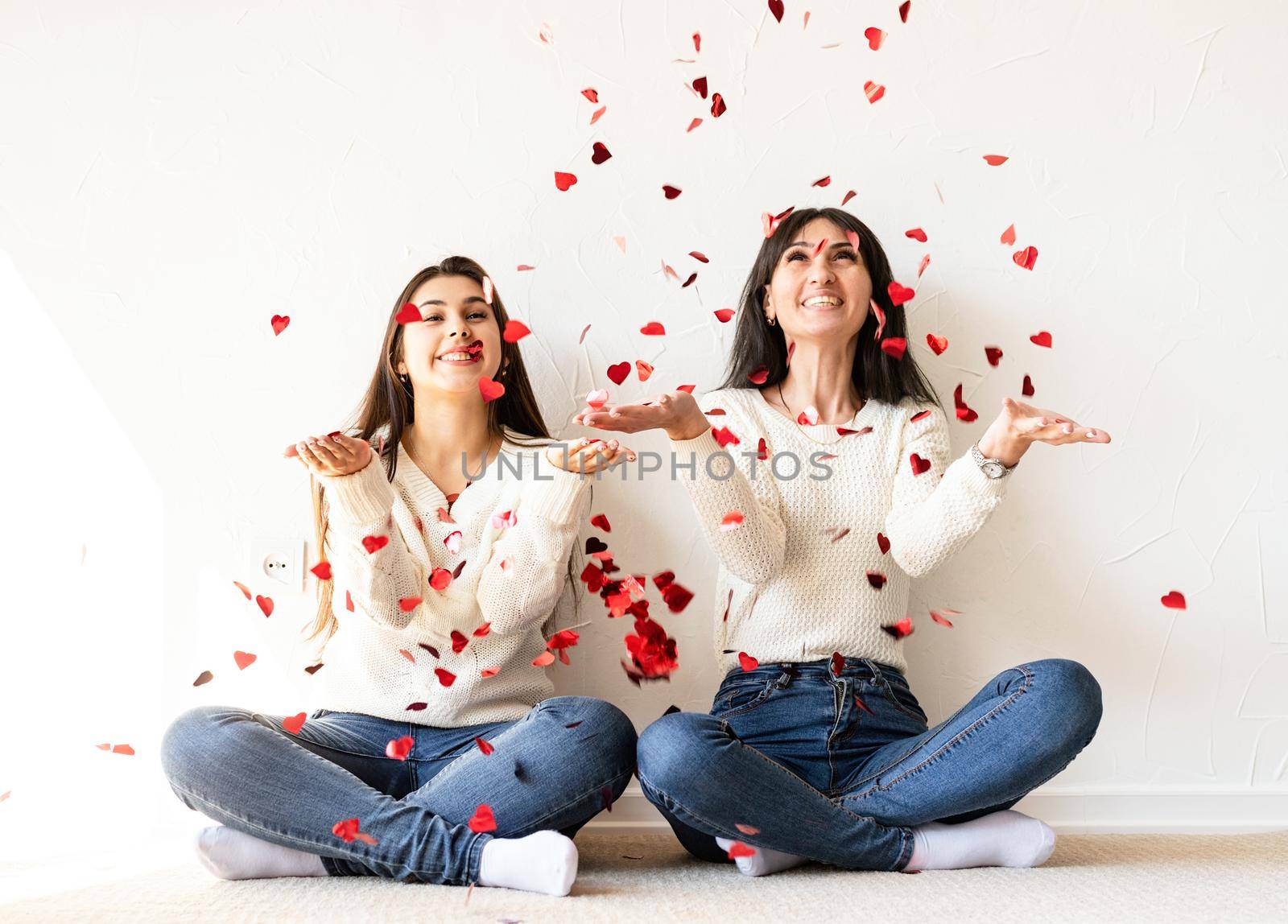 Two best friends having fun at home blowing red heart shape confetti