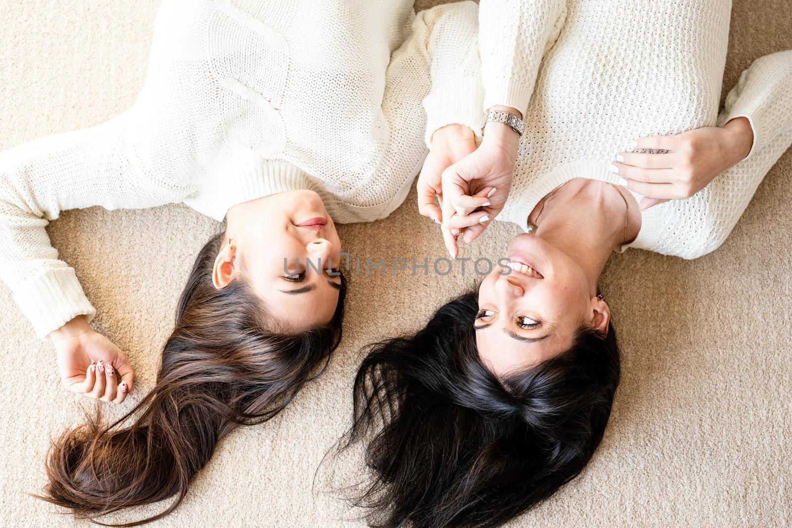 Two best friends laying on the rug at home talking by Desperada