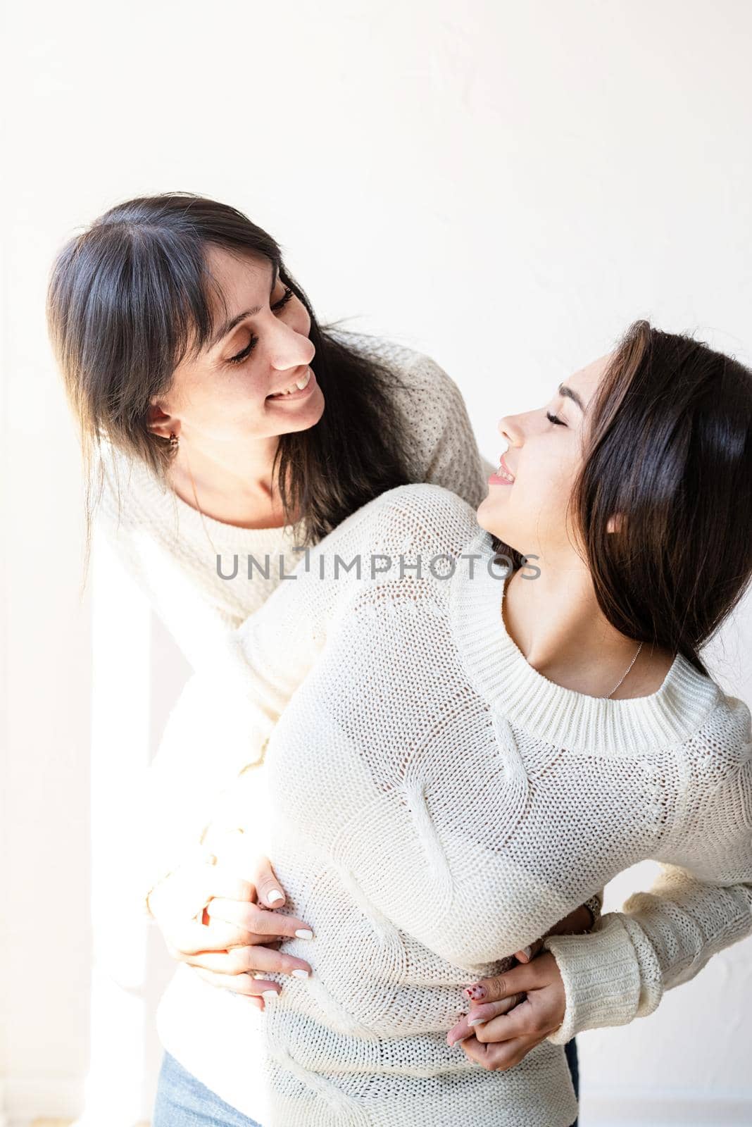 Two female best friends embracing each other standing on white background
