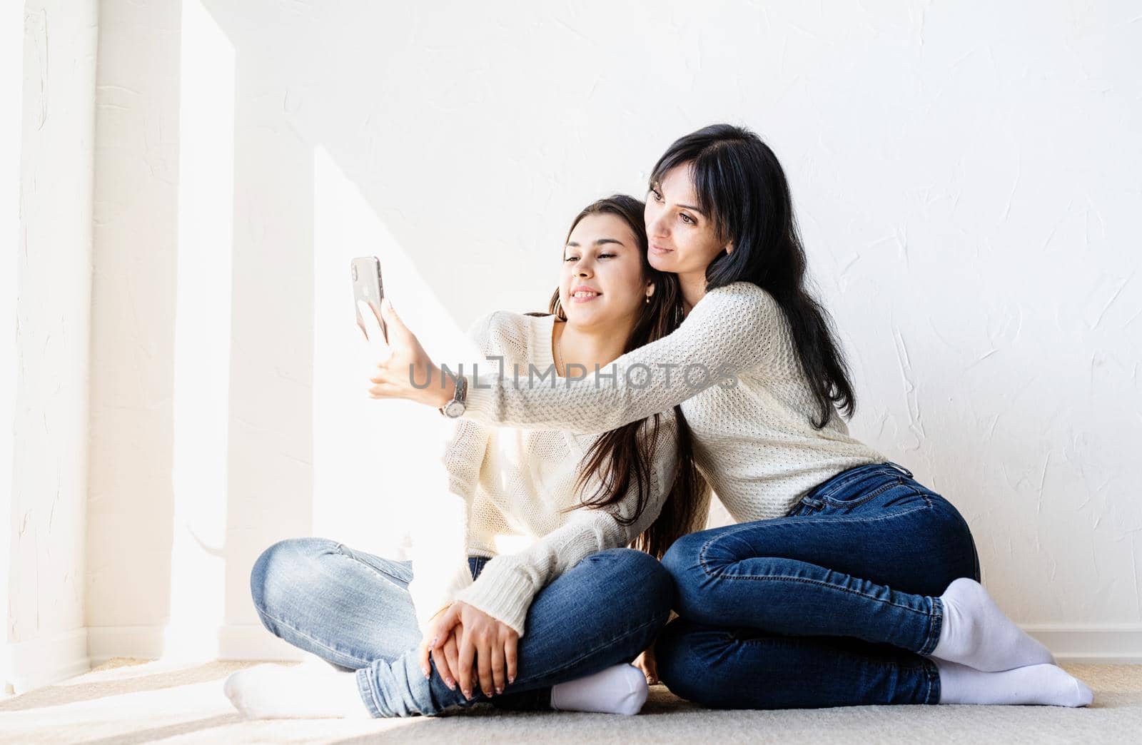Two beautiful women taking selfie on mobile phone making funny faces by Desperada