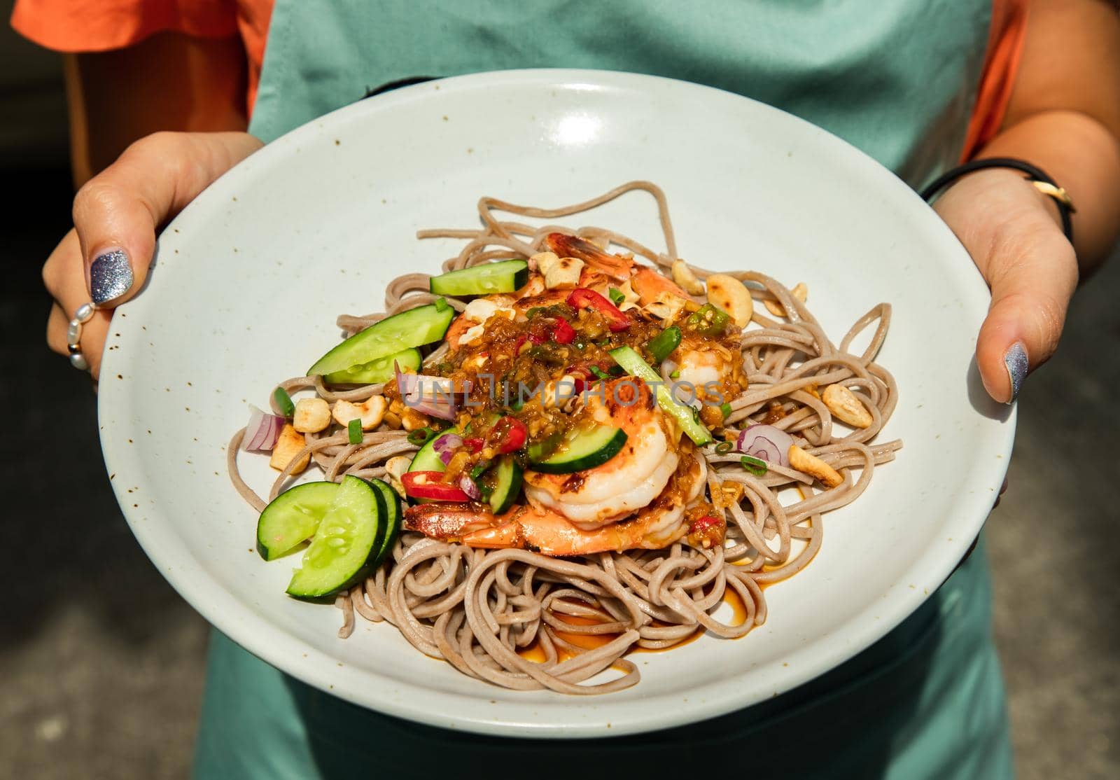 Close up of young woman hands showing udon and prawn spicy salad bowl. Healthy eating food, Selective focus.