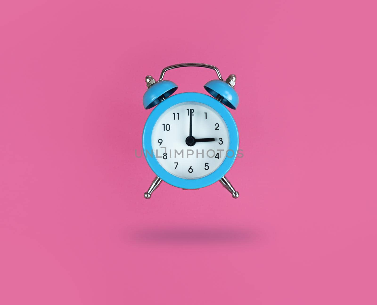 Levitating blue alarm clock on a pink background.