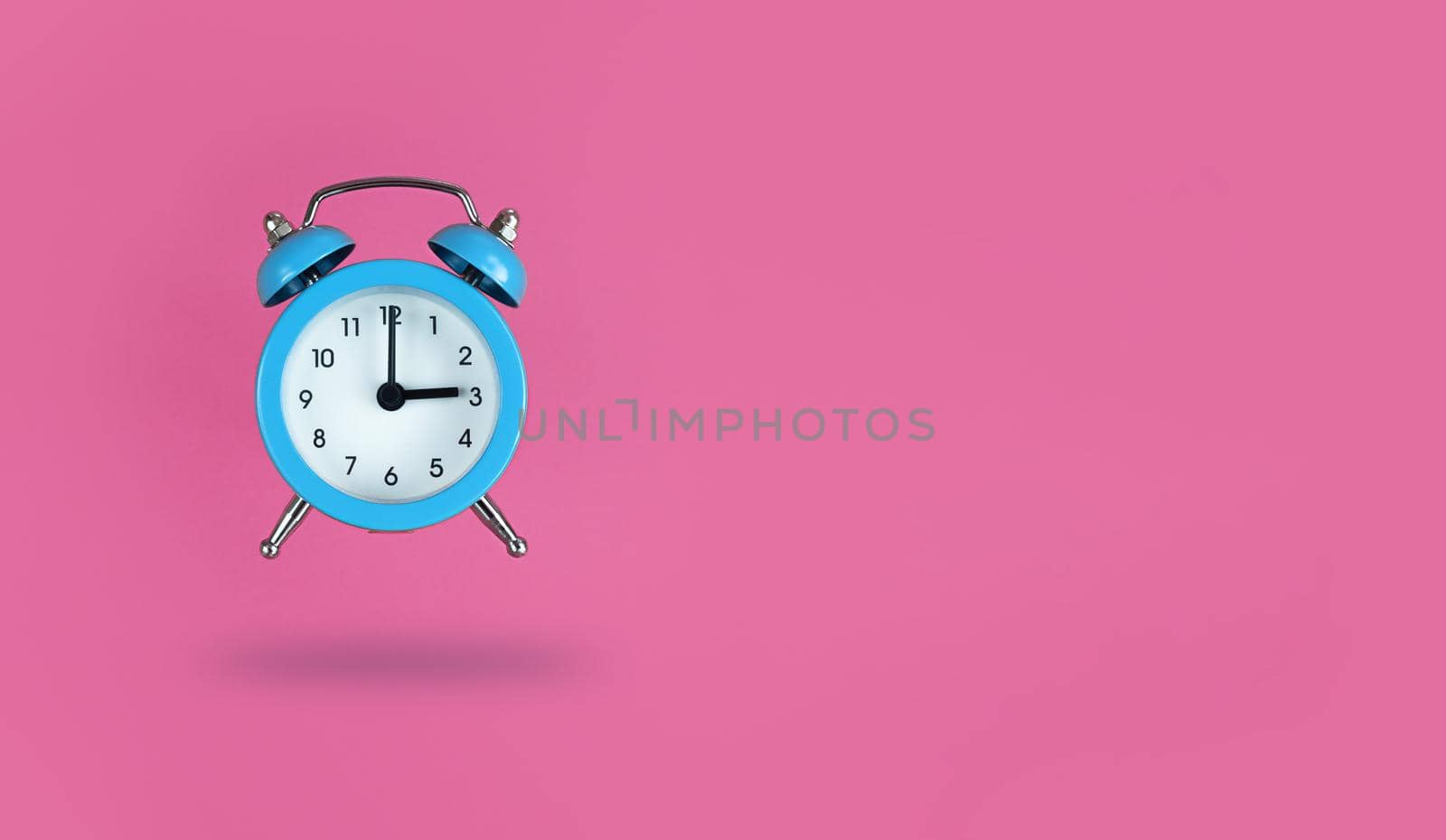 Levitating blue alarm clock on a pink background with copy space.