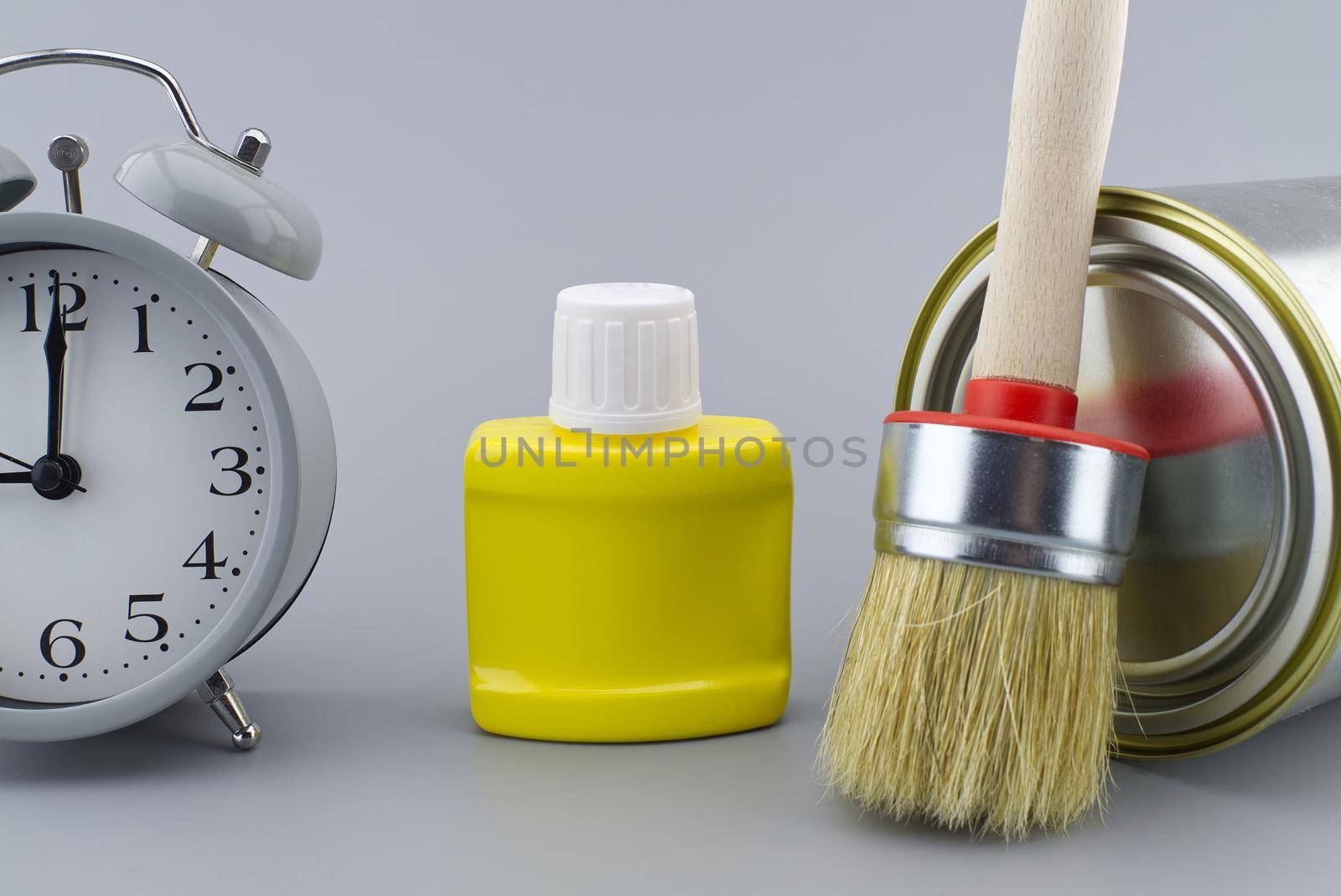 DIY, decorating or renovations concept with a still life of an alarm clock with assorted clean paint brushes and unlabeled tin of paint over a grey background