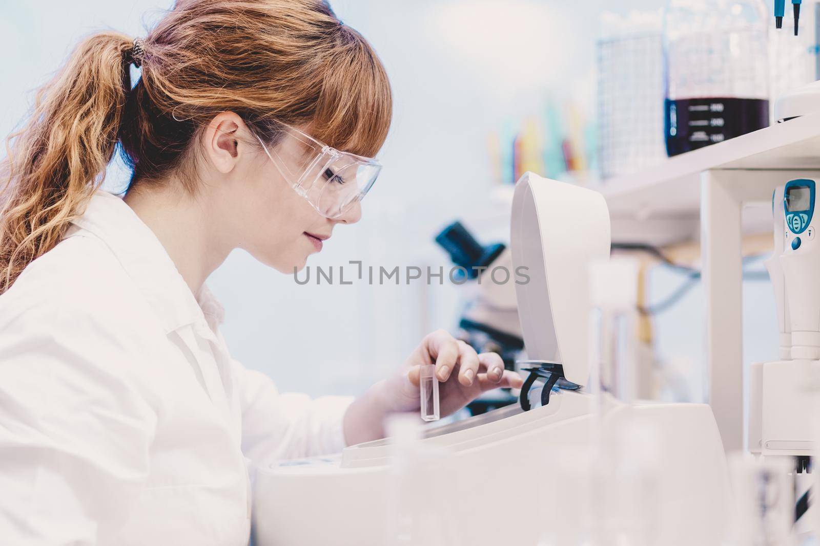 Focused attractive young life science professional measuring the absorbance of the solution in cuvette in the spectrophotometer. Focus on the researcher's face.