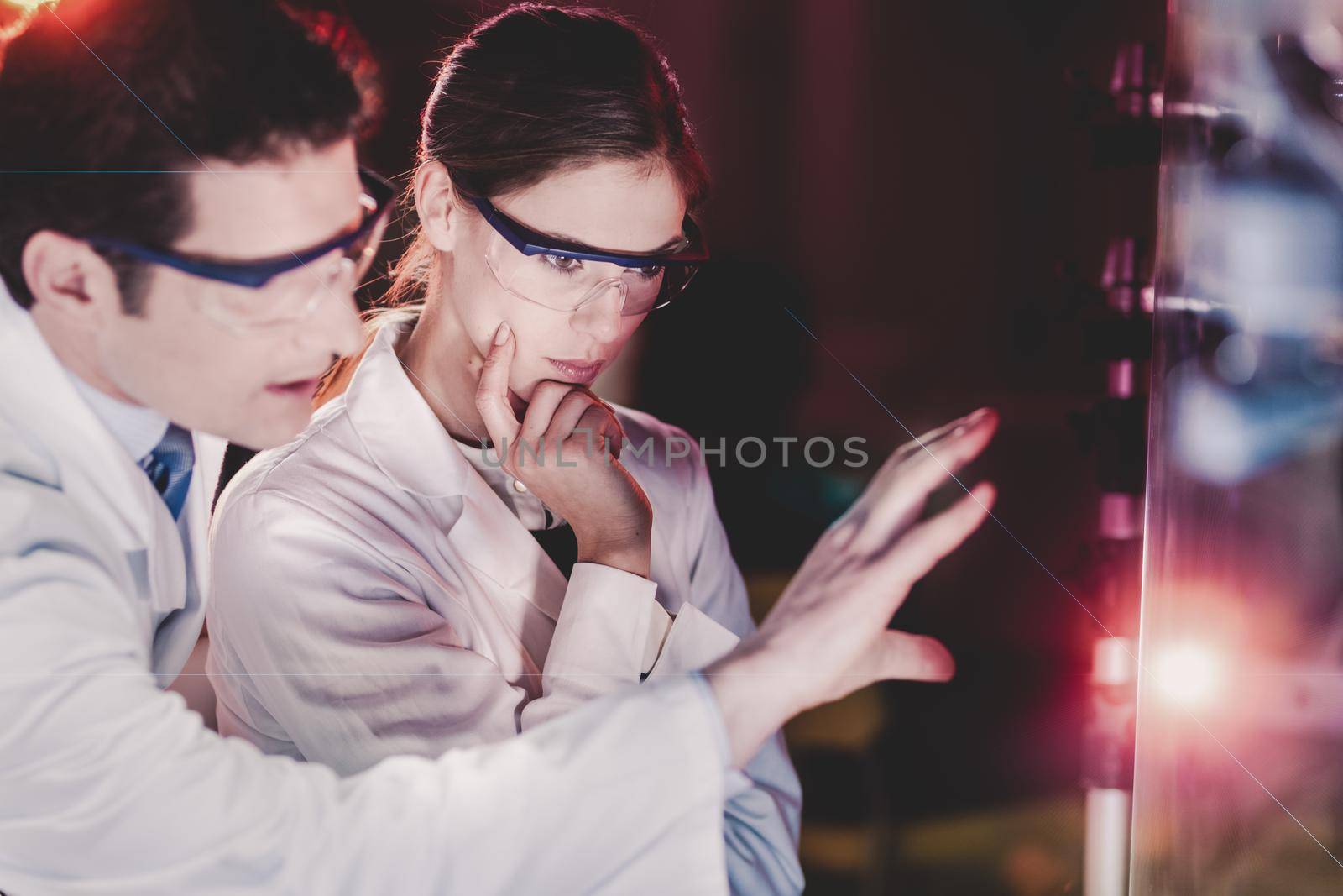 Portrait of a focused electrical engineering researchers in their working environment checking the phenomenon of breaking laser beam on the glass surface.