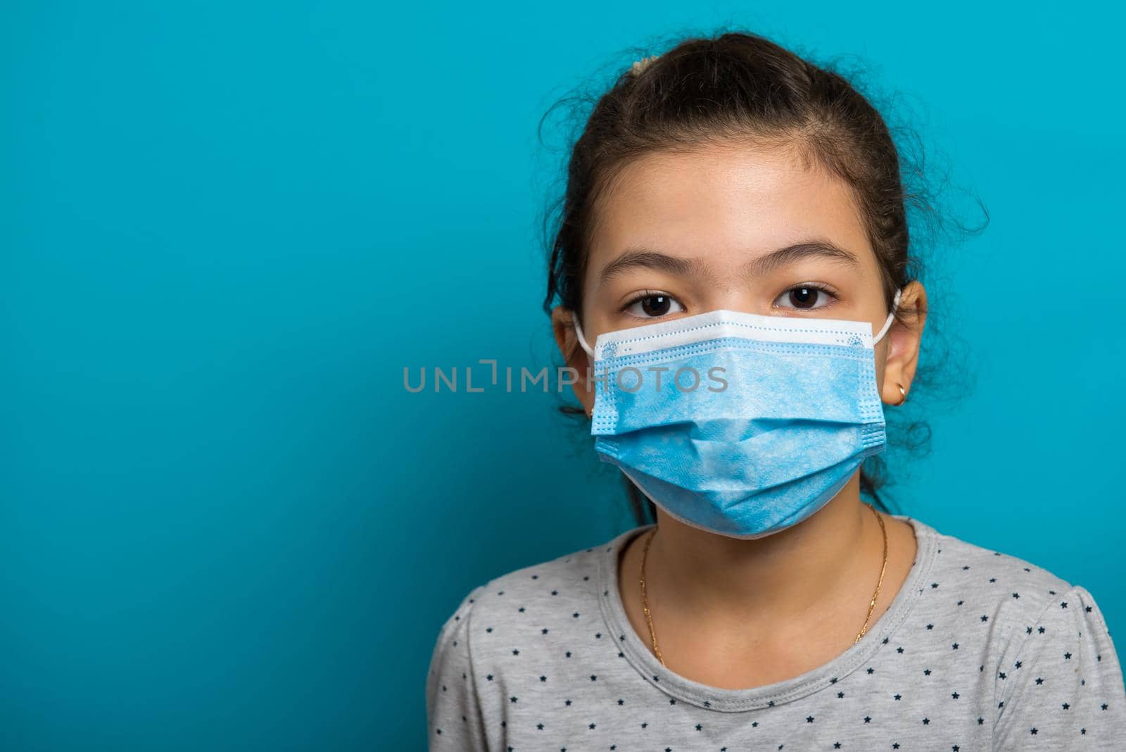 Arabian toddler girl in medical mask on blue background. Close-up.