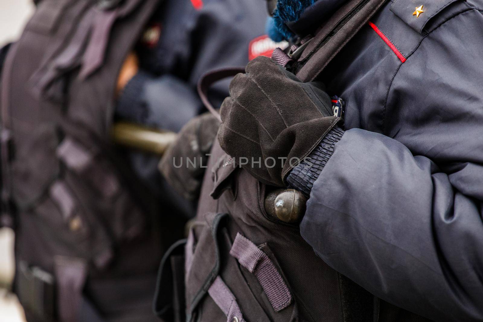 Tula, Russia - January 23, 2021: Police officers in black uniform with bulletproof vests - close-up view on black gloves with background blur.