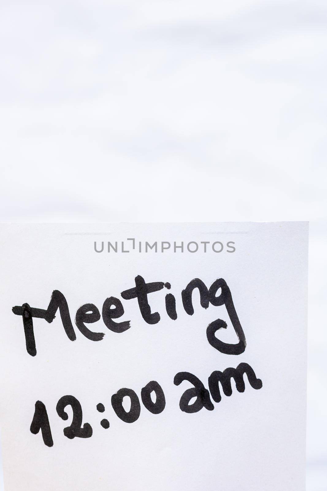 Meeting handwriting text close up isolated on white paper with copy space. Writing text on memo post reminder by vladispas