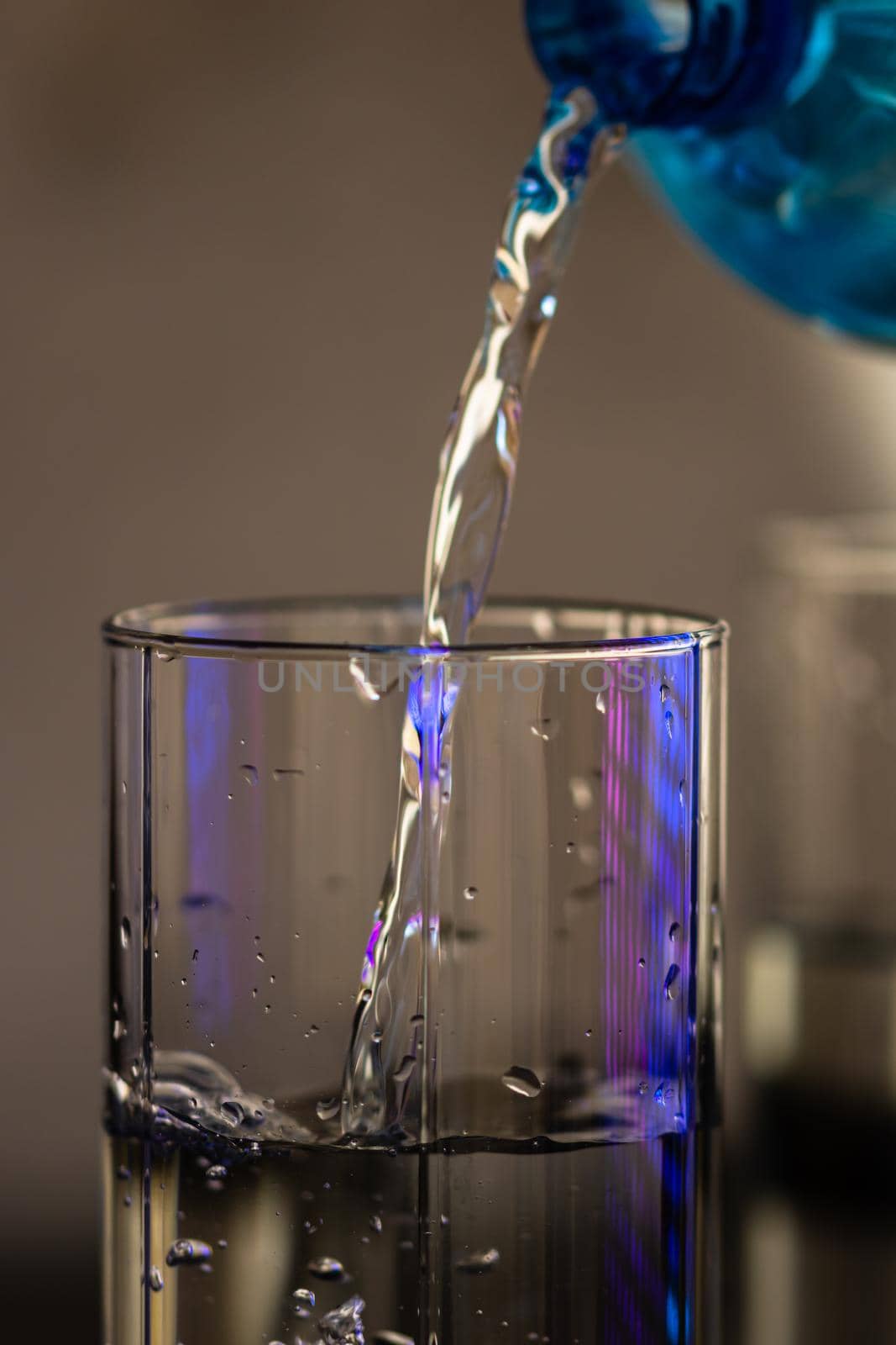 Pouring water from blue plastic bottle into a glass on blurred background. Selective focus, shallow DOF and copy space by vladispas