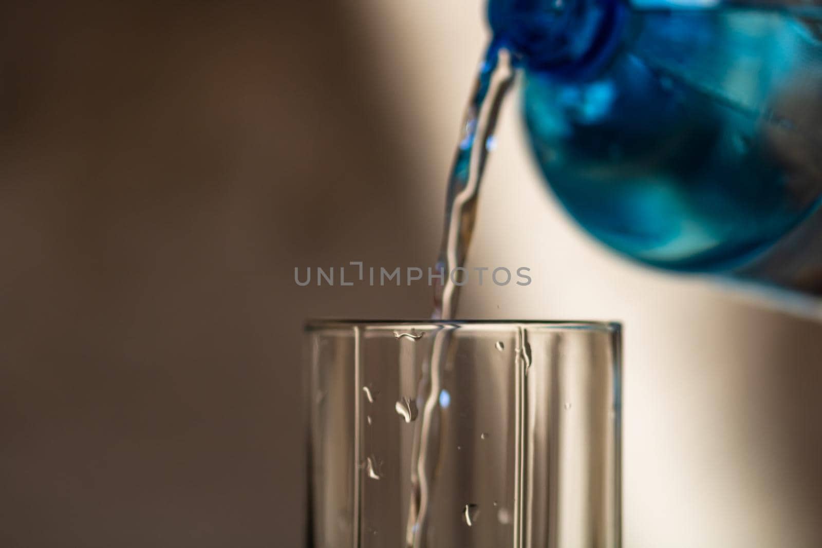 Pouring water from blue plastic bottle into a glass on blurred background. Selective focus, shallow DOF and copy space