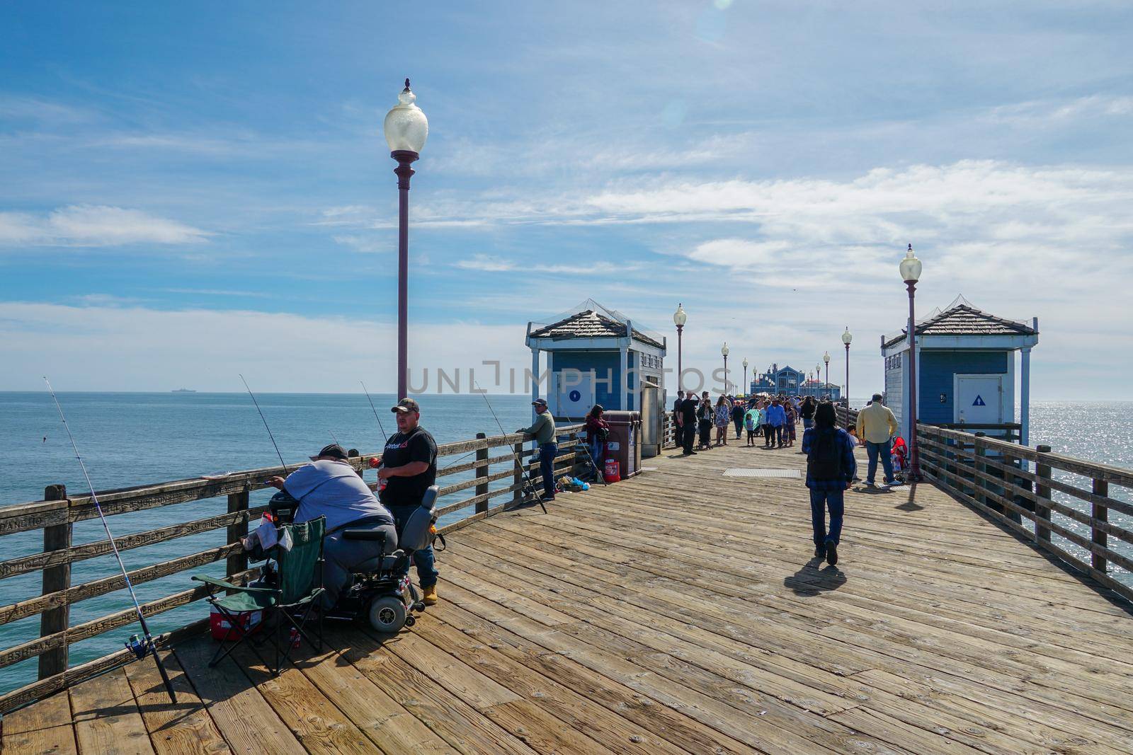 Tourist walking on the Oceanside Pier during blue summer day, Oceanside, northern San Diego County, California. Wooden pier on the western United States coastline. Famous for fisher. March 22nd, 2020