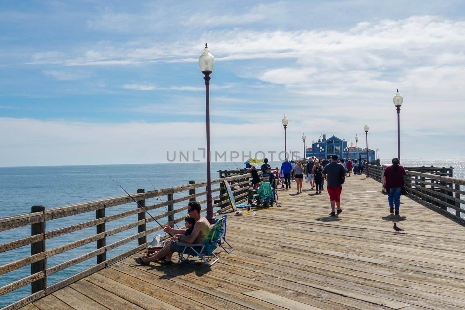 Tourist walking on the Oceanside Pier during blue summer day, Oceanside, northern San Diego County, California. Wooden pier on the western United States coastline. Famous for fisher. March 22nd, 2020