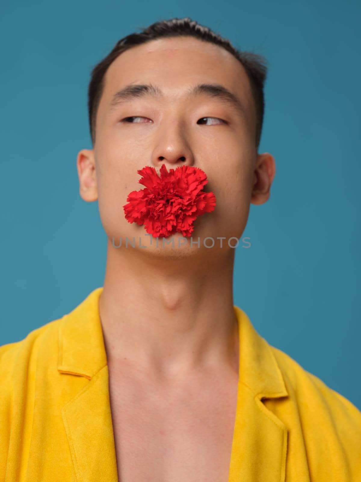 Portrait of a man with an Asian with a flower in his mouth on a blue background. High quality photo
