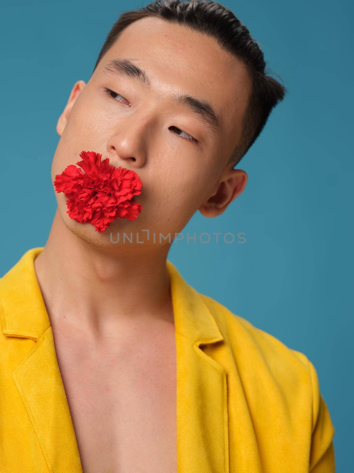 A man with a flower in his teeth on a blue background and an unbuttoned jacket. High quality photo
