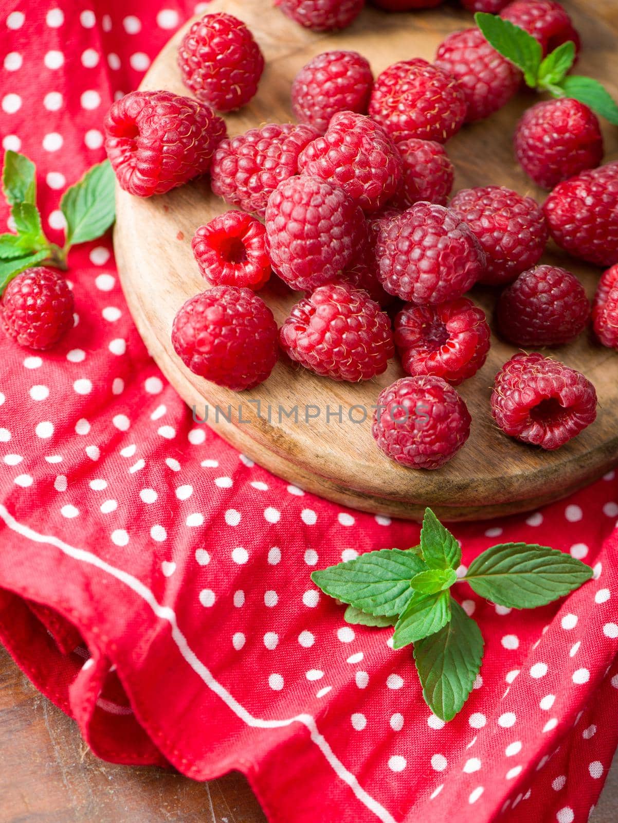 Ripe sweet raspberries in bowl on wooden table.