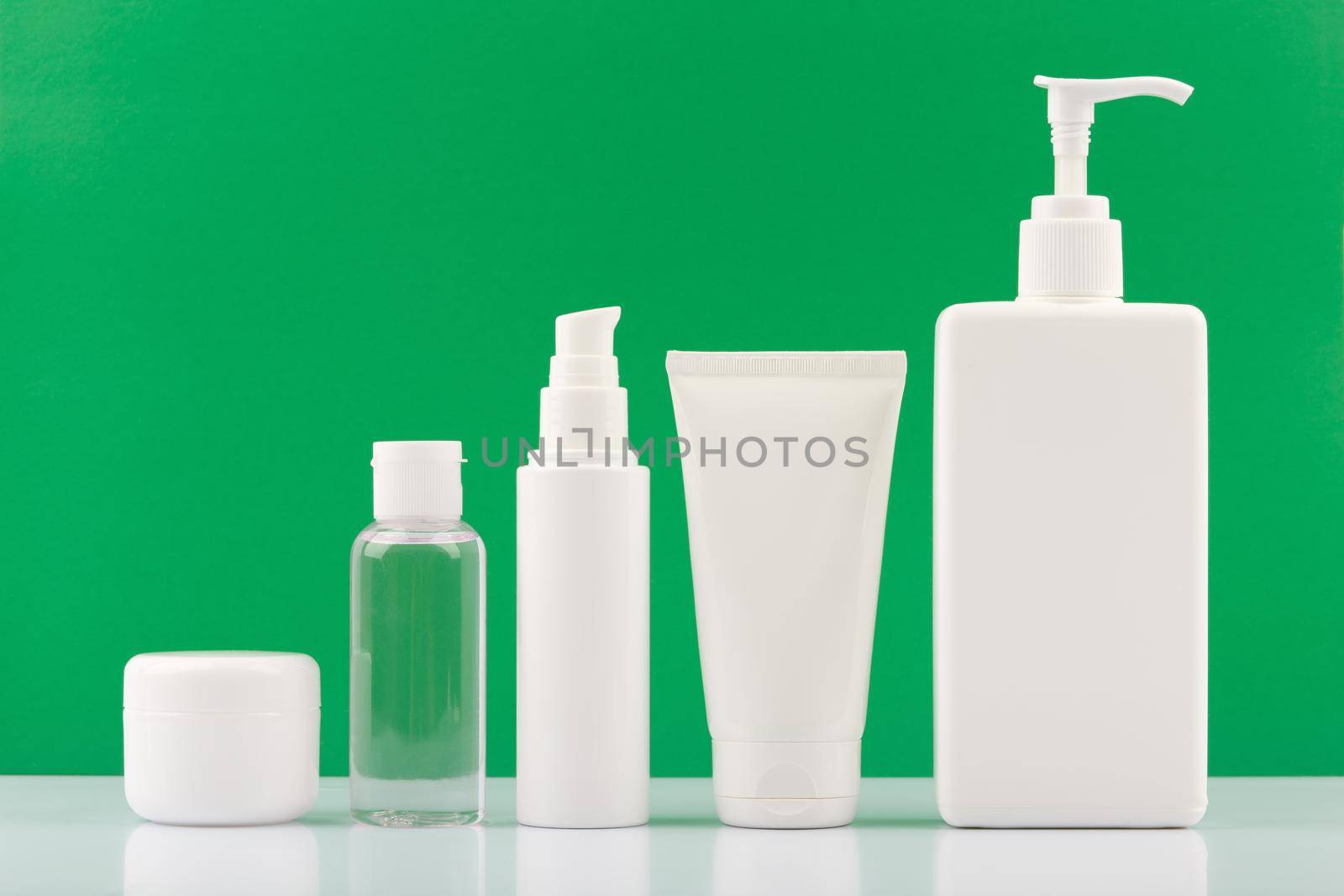 Set of cosmetic products with facial and body moisturizing cream or lotion, under eye cream, soothing lotion and facial cleaner on white table against green background. Concept of organic beauty 